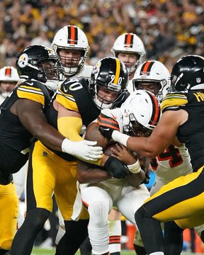 A football player in a black and yellow Steelers uniform is being tackled by multiple Cleveland Browns players during a game.