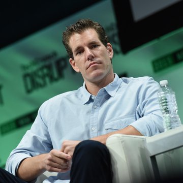 Cameron Winklevoss sits on stage at the TechCrunch Disrupt event, with the visible "DISRUPT" backdrop, as he discusses the AI-driven Bitcoin market and frames the current dip as an unprecedented buying opportunity.