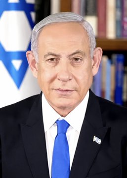 A portrait photograph of Israeli Prime Minister Benjamin Netanyahu wearing a dark suit and blue tie, with the Israeli flag and a bookshelf visible in the background.