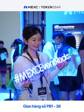 A promotional image showing a smiling young woman holding a "#MEXCEventPods" sign at a MEXC | TOKEN 2049 event, with text reading "Gian hàng số PB1 - 36" at the bottom.