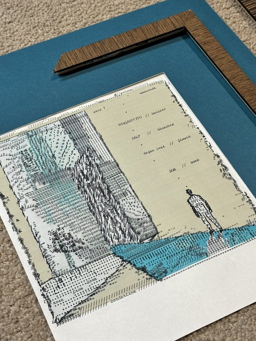 A framed artwork with a wooden frame corner visible, featuring an architectural drawing or map with cyan/turquoise accents and a small figure illustration, resting on a blue mat.
