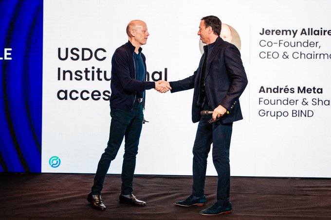 Two men shake hands on stage at a corporate event, with on-screen text identifying them as Jeremy Allaire (Co-Founder, CEO & Chairman of Circle) and Andrés Meta (Founder & Shareholder of Grupo BIND), alongside the announcement "USDC Institutional access," reflecting Circle's partnership expansion of $USDC stablecoin access to Argentina through Grupo BIND.