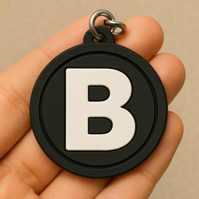 Close-up photo of a black circular keychain or pendant with a large white letter "B" held in a person's hand.