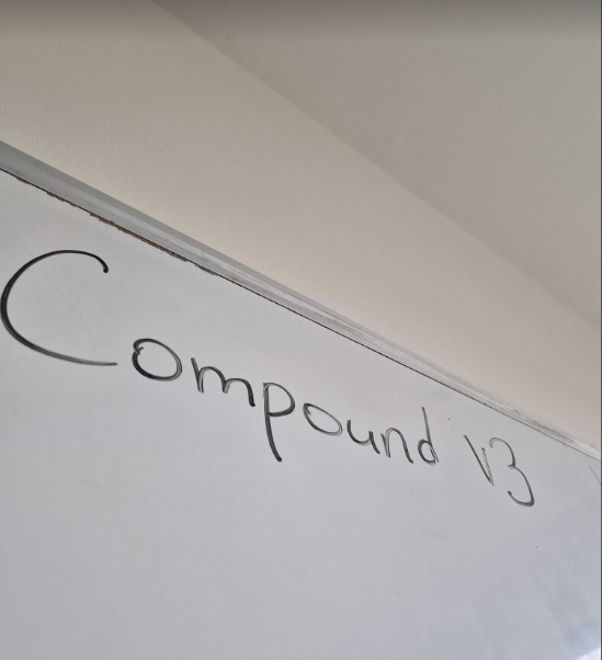 Handwritten text on white paper reading 'Compound 1/3' taped to a ceiling or wall.