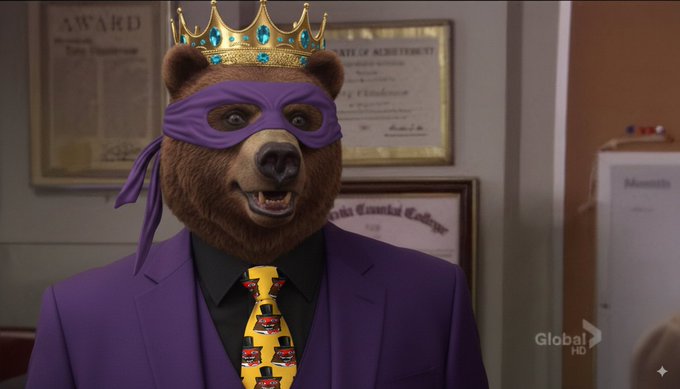 A brown bear mascot wearing a gold crown, purple eye mask, and a purple suit with a yellow tie featuring what appear to be XRP logos stands in an office with framed certificates on the wall behind him; a "Global HD" logo is visible in the corner. The image connects to the post's playful "back to work" declaration by portraying the $BEAR/XRPL mascot as a "king" returning to his throne, blending the heraldic crown with the bear branding to reinforce the comeback theme.