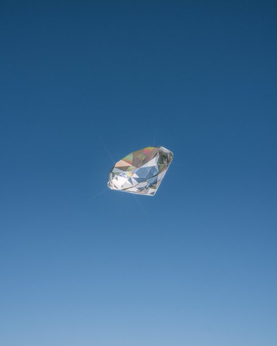 A 3D rendering of a faceted metallic gemstone, likely a diamond, floating against a clear blue sky.
