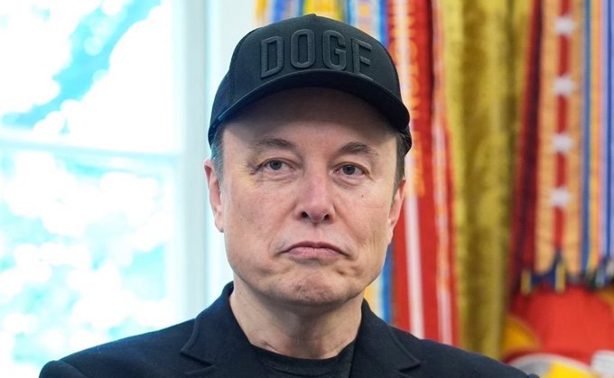 A man wearing a black "DOGE" cap appears in front of colorful flags, accompanying a quote from Elon Musk about Bitcoin being "based on energy" and impossible to fake. The image illustrates Musk, the advocate behind the Dogecoin cryptocurrency referenced on his hat, discussing his views on Bitcoin's energy-based foundation.