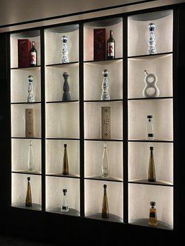 A backlit display shelving unit featuring an assortment of decorative bottles, vases, and boxes arranged in individual cubbies, with soft interior lighting highlighting each item.