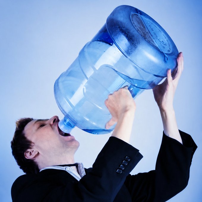 A man in a dark suit tilts his head back, drinking directly from an oversized blue water jug. The image humorously reinforces the post's message about interns taking hydration breaks during trading.