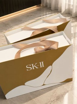 Two elegant gold and white SK-II gift bags with satin ribbon handles sit on a marble surface, likely the luxury skincare gift from the Hangzhou crypto executive mentioned in the post.