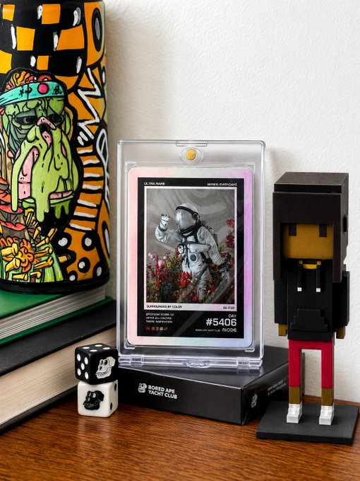 A small curated display of crypto collectibles: a Bored Ape Yacht Club card series featuring astronaut "Ultraknowledge" (#5406) sits in a protective slab alongside an orange patterned Ape figurine, a Papercraft 8Bit Ape figure, and DICE dice—all arranged as a compact "web3 corner" that fits within the limited space allotted.