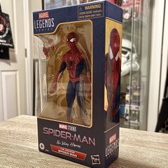 Photograph of a packaged Marvel Legends Series Spider-Man action figure in its window box, labeled with a yellow 'WARNING' sticker on top, displayed on a wooden surface.