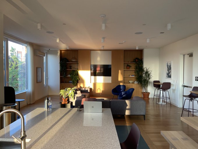 A sunlit, modern lounge area with wooden shelving, plants, and a central couch. The post discusses Bitcoin Archive's founder Archie's two-hour interview, though no interview content or text is visible in the image.