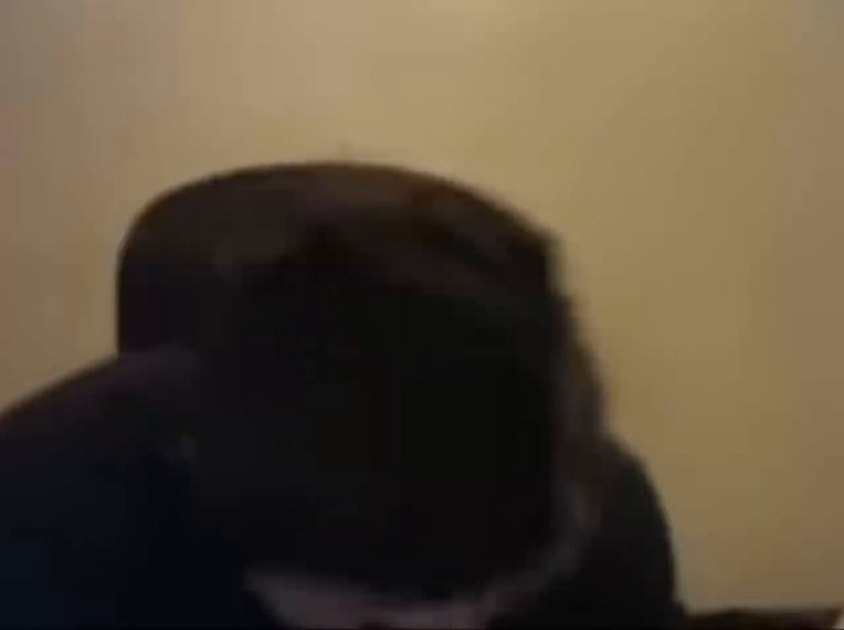 The image shows a person wearing a black hat, sitting down with their head tilted back. They are looking at something off-camera, possibly engaged in an online video call or browsing content on social media platforms. The background of the image appears to be a wall, and there is text that reads "$TIBBIR FUAAAARK". This suggests that the person might have been watching a video or reading an article related to the $TIBBIR FUAAAARK theme.