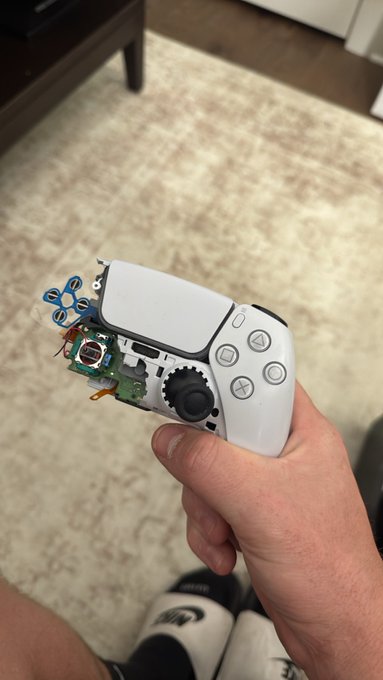 A hand holds a partially disassembled white PlayStation 5 DualSense controller, exposing the internal circuit board and components, while the caption "About to pull the fleece of the century" suggests the controller is being parted out to sell its internal components for profit.