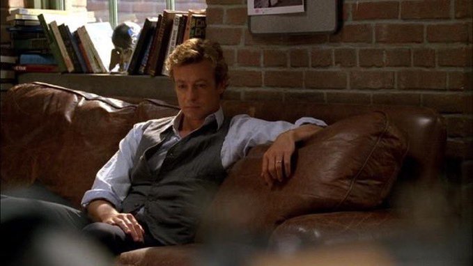 A man in a vest and dress shirt sits on a brown leather couch looking worn and distressed, with books visible on a shelf behind him and a small statue on the windowsill. The image's caption references someone's dwindling ability to handle small financial transactions, suggesting the man's tired, contemplative expression reflects the mental fatigue of repeated small spending.