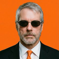 A serious-looking man with a gray beard, wearing dark sunglasses, a black suit, and a bright orange tie against an orange background. The image appears to depict Michael Saylor, the founder of Strategy (formerly MicroStrategy), whose company joining the world's top 500 most valuable companies is the focus of the celebratory post.