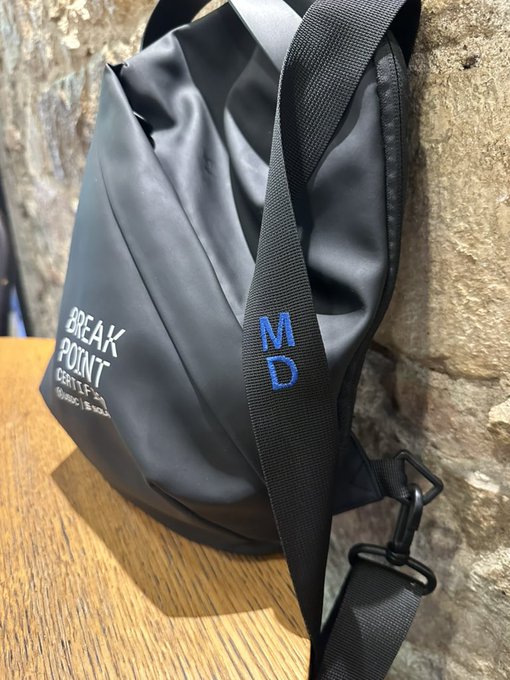A black waterproof roll-top bag sits on a wooden surface, featuring the text 'BREAK POINT' and 'MD' printed on its strap.