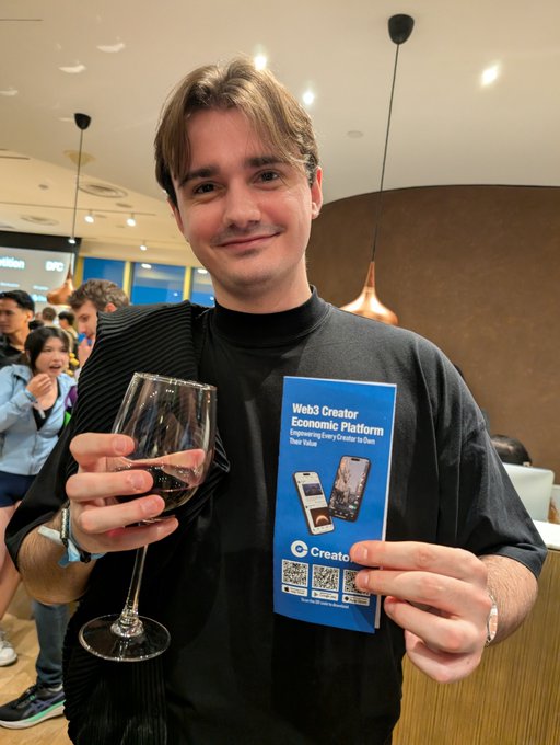 A young man smiling while holding a wine glass in one hand and a blue 'eCreator' promotional card for 'Web3 Creator Economic Platform' in the other.