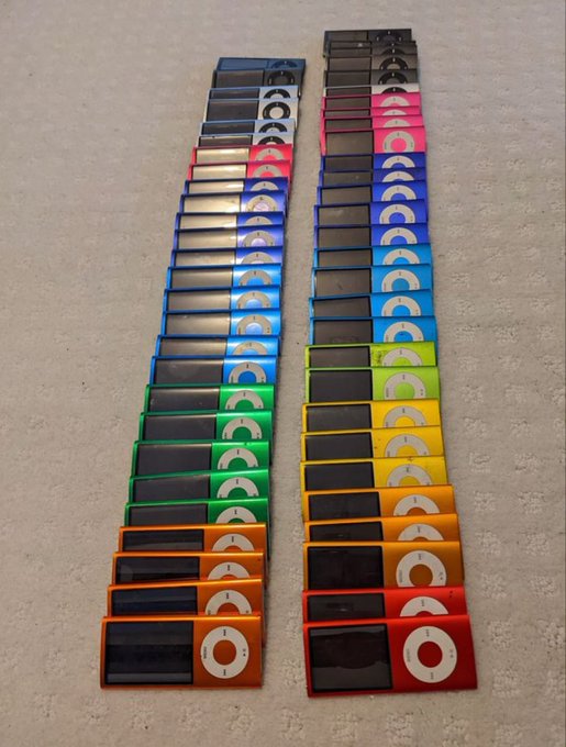 Two rows of colorful iPod Nano devices in various shades (orange, red, yellow, green, blue, purple, pink, black) are lined up on a floor.