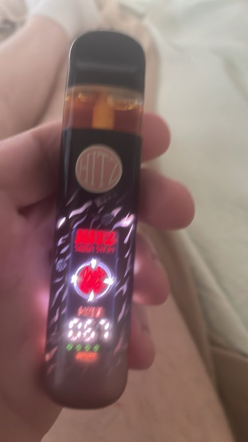 A hand holds a black and red vape pen with the 'HITZ' logo illuminated, showing a digital display reading '6.6V' and the text 'BITZ' on its body.