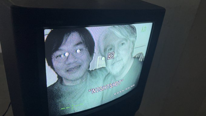 An old CRT television displays a grainy green-tinted image of two faces with the text '"NIGHTSHOT"' and camera overlay graphics on the screen.