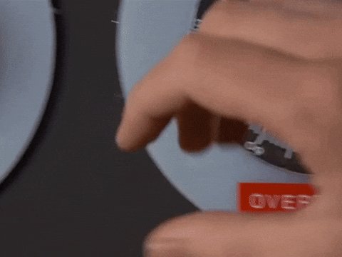 The image shows a person's hand pointing towards an oven with a red "OVER" sticker on its door, indicating that the oven has been used recently or is ready for use. The background of the photo appears to be black, which contrasts with the white plate and the oven door.