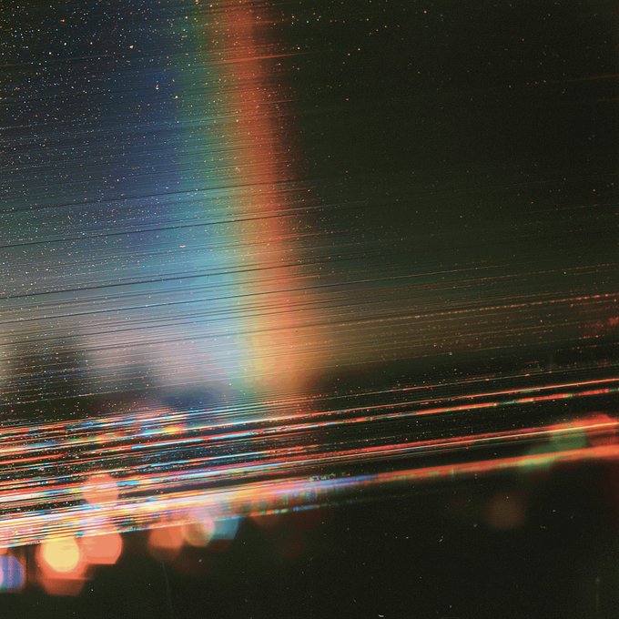 An abstract image featuring streaks of light in vibrant blues, greens, oranges, and reds against a dark background, with bokeh effects at the bottom.