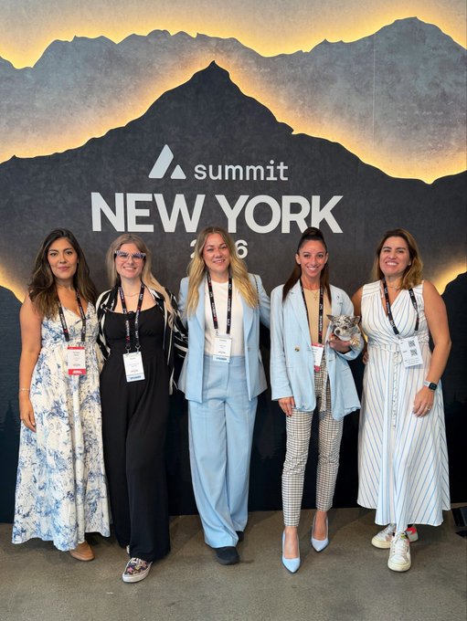 Five women wearing lanyards pose in front of a 'Summit New York 2026' mountain-themed backdrop.