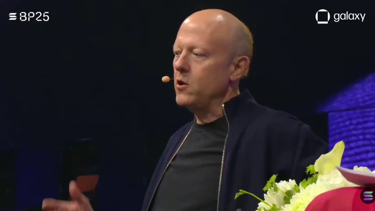 The image shows a man speaking into a microphone, with a large screen behind him displaying the text "@CIRCLE CEO- ?". The focus of the image seems to be on the speaker's words rather than his appearance or surroundings.