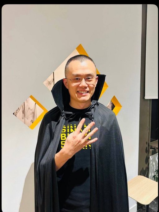 A man with glasses smiles and holds up three fingers while wearing a black cape and a T-shirt reading "BIN LADEN" in yellow letters, fitting the playful "wrong answers only" prompt by humorously suggesting he might be the infamous figure himself.