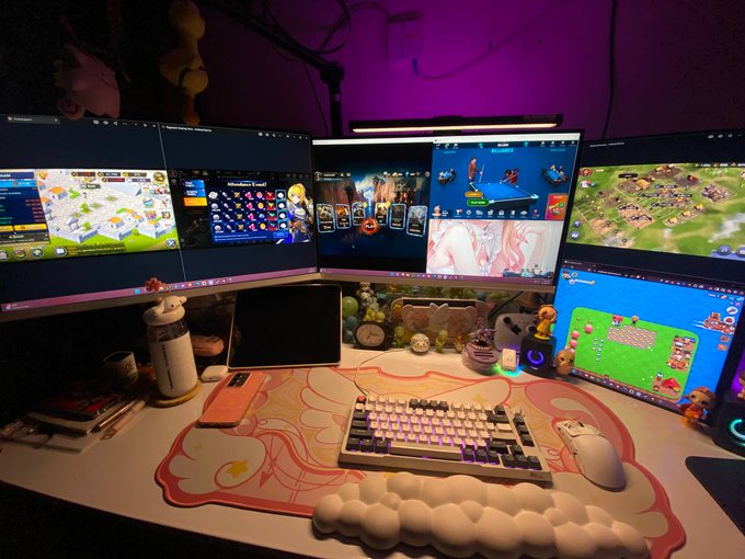 A multi-monitor gaming/gaming setup with at least 6 screens displaying various games, a mechanical keyboard, white mouse, cloud-shaped wrist rest, and small plush toys in a purple-lit room.