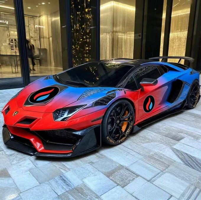 A red and blue gradient Lamborghini Aventador sports car parked in front of a modern building with a Christmas tree visible through the glass windows.