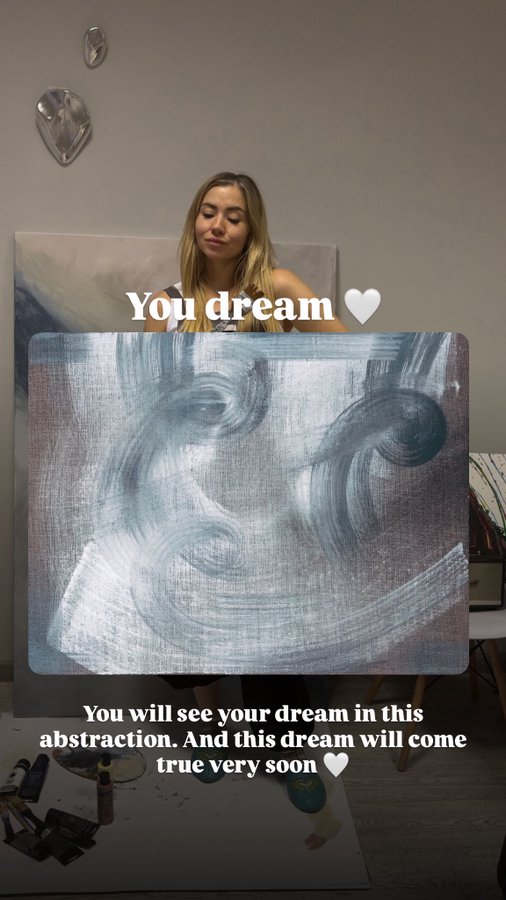A young woman stands behind an abstract blue and white painting, with text overlay reading 'You dream 🤍 You will see your dream in this abstraction. And this dream will come true very soon 🤍'.