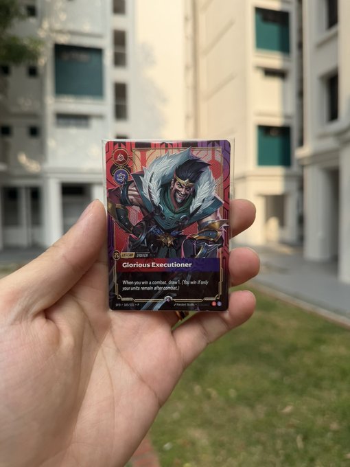 A hand holding a League of Legends trading card titled 'Glorious Executioner' featuring the champion Darius, photographed outdoors with a building and grass visible in the background.