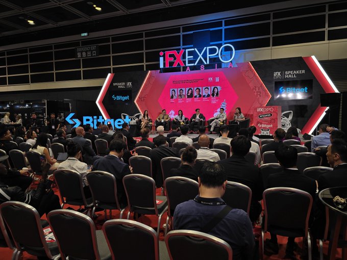 A panel discussion takes place at the iFX EXPO Asia 2025 Speaker Hall, sponsored by Bitget, with a moderator and several speakers seated on stage facing a seated audience.