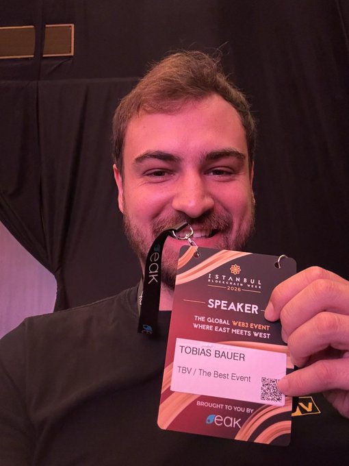 The image features a man wearing a black shirt with a name tag that reads "TBV BAUER" and holding up his name tag, which has a picture of him smiling. The background appears to be a dark room or stage setting, suggesting an event or gathering. The text in the image includes phrases such as "First day here in Istanbul!", "Most conversations are about RWA", "Law No. 7988, CMB, MASAK regulated crypto for holding, buying, selling and trading but not for payment to protect financial stability.", and "Focus on what is in the image and how it relates to the post".