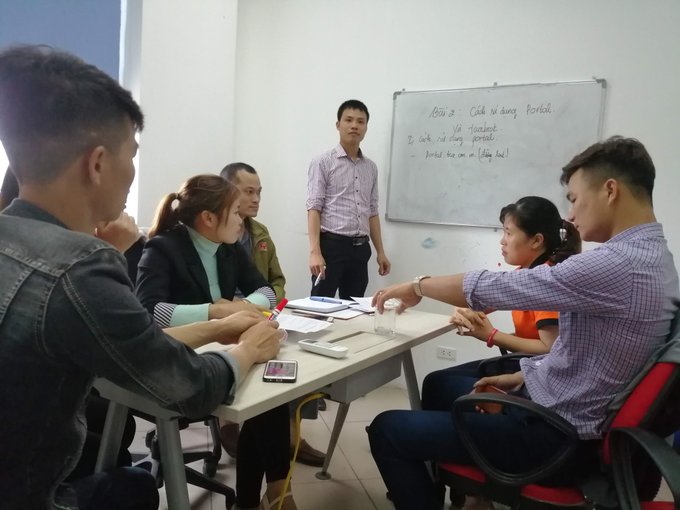 A group of people gathered around desks in a classroom setting, with a man standing by a whiteboard displaying 'Cách sử dụng fordata' and instructions for 'Trắc nghiệm' and 'Tổng hợp'.