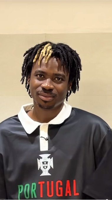 A young man with dreadlocks featuring blonde highlights smiles while wearing a black and white Portugal soccer jersey.