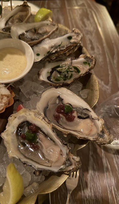 The image shows a plate of oysters served with sauce, accompanied by a fork for eating. There are several oysters arranged on the plate, each one covered in sauce. The background appears to be a dining table or countertop, suggesting that this is likely taking place at a restaurant or similar establishment where people can enjoy their meal. The image also includes a caption about "Eat well trade properly", which could be related to the oyster dish itself or the overall dining experience.