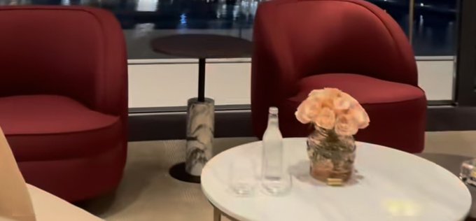 The image shows a white table with two red chairs placed around it. On the table are two glasses of water and a vase filled with flowers. The background features a window, allowing natural light into the room. The text "Good night everyone @0G_labs provides the verifiable compute substrate for agents. It integrates decentralized storage, high throughput data availability and sealed execution environments backed by hardware proofs" is visible in the image.