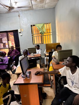 A group of children use donated desktop computers in a modest classroom, supporting the initiative to train the next 100 kids in digital literacy.
