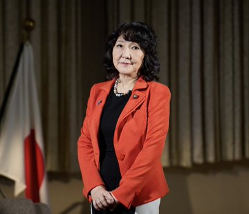 Satsuki Katayama, Japan's Finance Minister, stands in a red blazer in front of a Japanese flag, as she announces plans to legalize cryptocurrency ETFs in Japan.