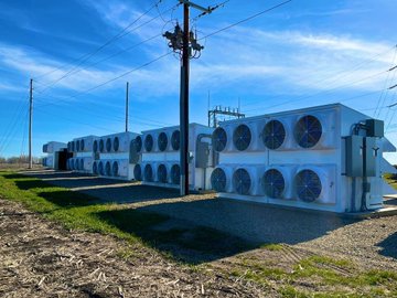 A row of large Bitcoin mining units with cooling fans operates outdoors under a power line in a cold, open landscape. The image illustrates the post's point about serious mining operations favoring northern climates, where natural cool air and abundant renewable energy make large-scale crypto mining more efficient.