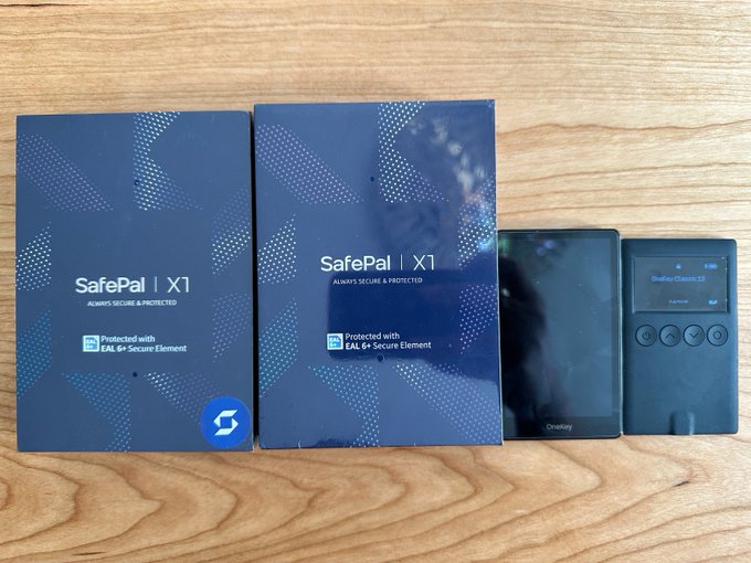Two SafePal X1 hardware wallet boxes (labeled "Always Secure & Protected" and "Protected with EAL 6+ Secure Element") sit beside their unpacked devices on a wooden surface, illustrating the issue of unverified tamper-evidence—since SafePal X1 packaging lacks the tamper-evident seals found on competitors like Ledger, buyers cannot easily confirm whether their newly purchased wallet is truly factory-fresh or has been compromised in transit.