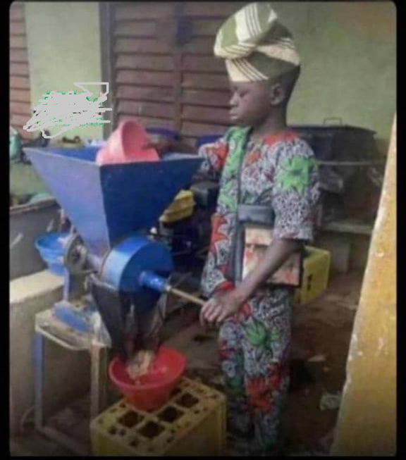 The image shows a young boy wearing traditional African attire, standing next to an open coffee grinder. He is grinding some beans into a red bowl placed inside the grinder. The image conveys a sense of nostalgia with the black and white photo editing making the boy appear older than his age. The caption below this image suggests that only $1k is needed to purchase fresh coffee in the state, which could indicate economic challenges or an antiquated system for distributing food items like coffee beans within the community.