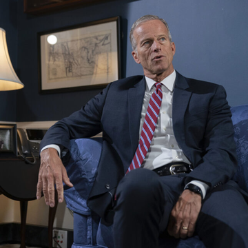 Senate Majority Leader John Thune, seated in a blue armchair wearing a navy suit and a red, white, and blue striped tie, speaks during an interview as he advances the CLARITY Act toward a cloture vote expected around September 14–15.