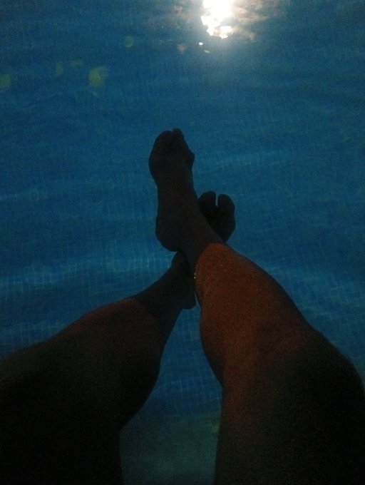 Two silhouetted legs extend toward the surface of an illuminated swimming pool at night, capturing a moment of tranquil escape. The image reflects the post's sentiment of letting go from past stresses, embodying the peaceful, carefree existence of someone living quietly off the grid.