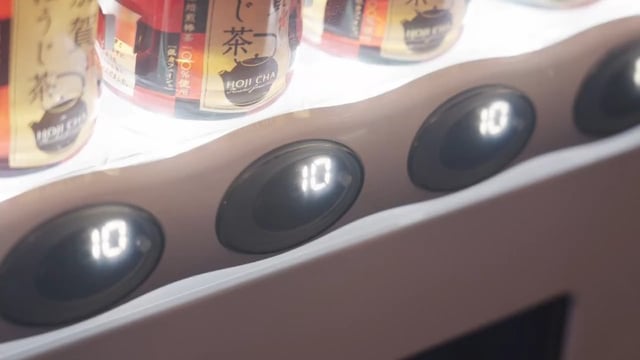 A close-up of a vending machine shows selection buttons displaying "10," with bottles of Itoen Oi Ocha tea (labeled with "お~いお茶" and Japanese text) visible in the upper portion, illustrating how stablecoins on the Sui blockchain are being integrated into everyday consumer transactions in Japan.