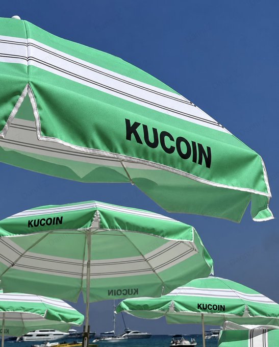 Beach umbrellas branded with the "KUCOIN" logo line a sunny seaside, matching the post's carefree "green skies, good vibes" caption and its invitation to tag a friend for a relaxing coastal view.